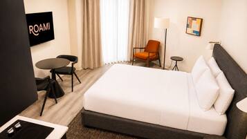 Una habitación de hotel con cama, escritorio, silla, televisión y lámpara.