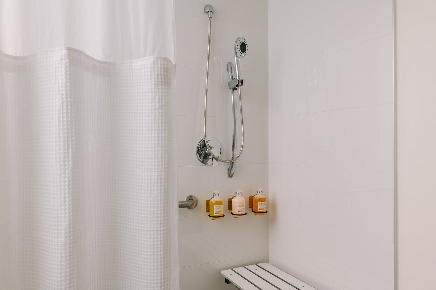 A bathroom with a shower, a towel rack, and a shelf with toiletries.
