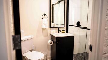A bathroom with a toilet, sink, mirror, and shower.