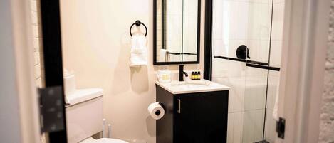 A bathroom with a toilet, sink, mirror, and shower.