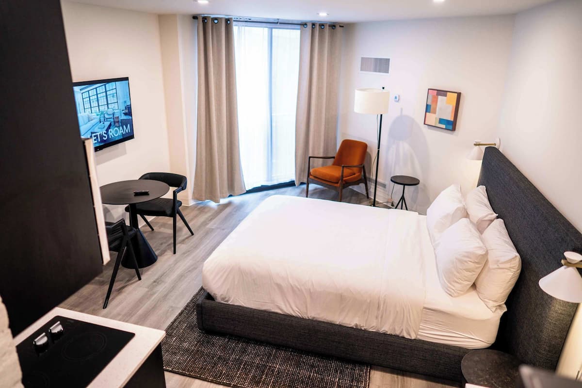 Een hotelkamer met een bed, een bureau, een stoel, een televisie en een raam met gordijnen.