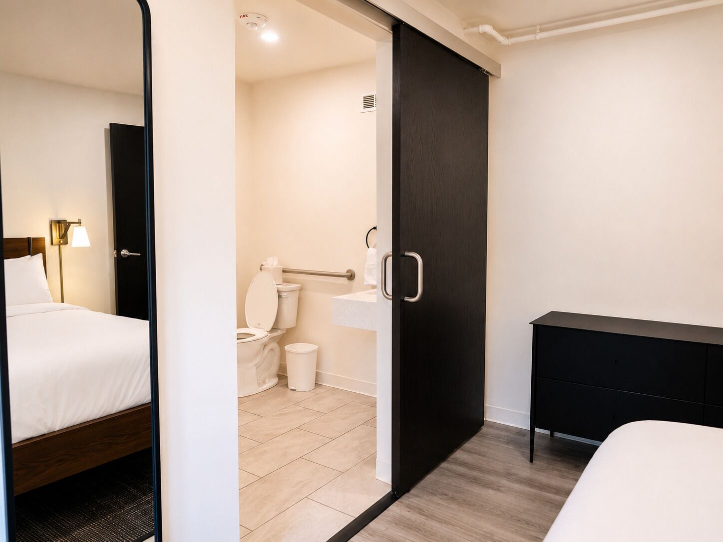 A hotel room with a bed, a bedside table, a desk, a toilet, and a shower area.