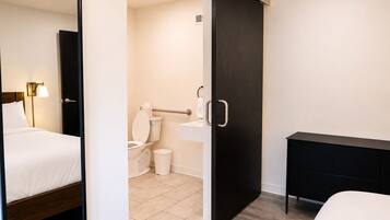 A hotel room with a bed, a bedside table, a desk, a toilet, and a shower area.