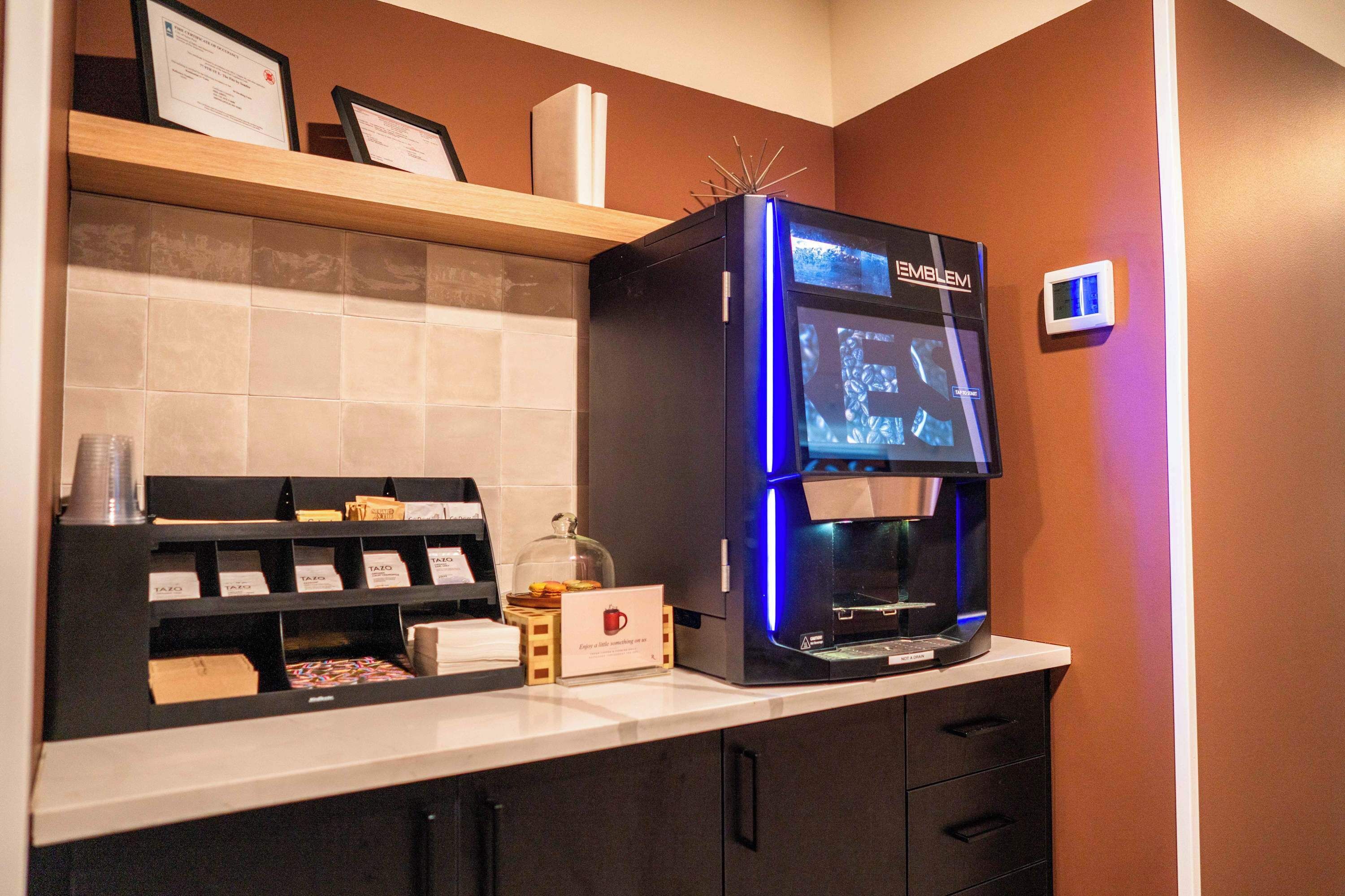 A coffee machine with a digital display, a coffee cup, and a menu board in a hotel setting.