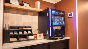 A coffee machine with a digital display, a coffee cup, and a menu board in a hotel setting.