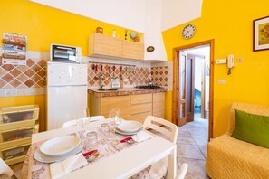 Una cucina compatta con forno a microonde, fornelli e pensili in legno. Un tavolo da pranzo è apparecchiato con piatti e bicchieri.