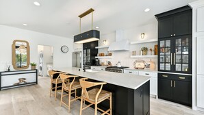 A modern kitchen with a large island, bar stools, and black cabinetry. - Gorgeous 3-bedroom lakefront house with AC on charming Big Cedar Lake! (West Bend)
