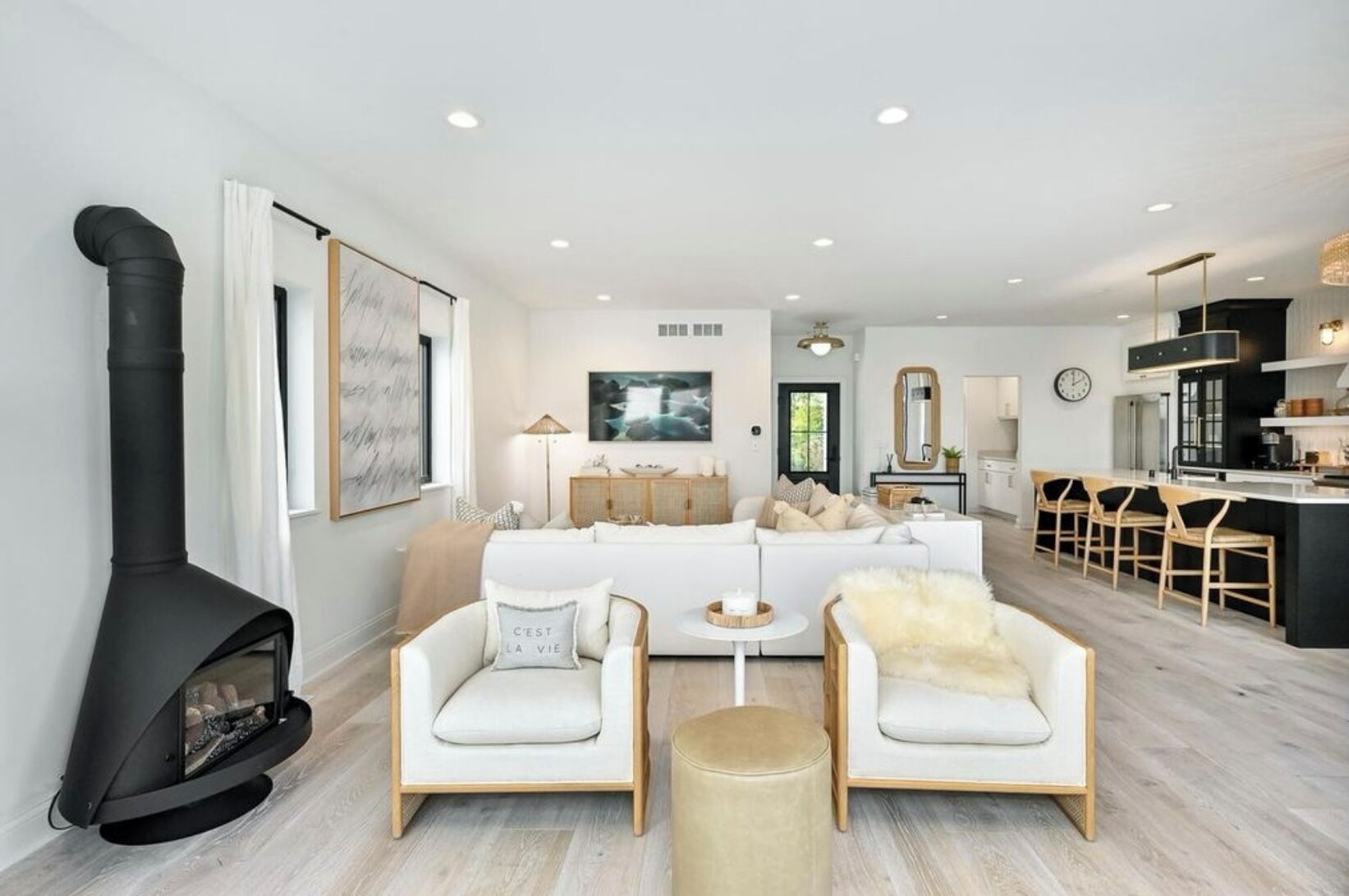 A modern living room with a fireplace, a sofa set, and a kitchen area with bar stools.