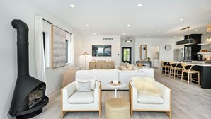 A modern living room with a fireplace, a sofa set, and a kitchen area with bar stools. - Gorgeous 3-bedroom lakefront house with AC on charming Big Cedar Lake! (West Bend)