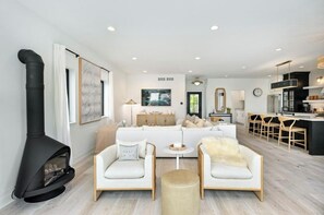 A modern living room with a fireplace, a sofa set, and a kitchen area with bar stools. - Gorgeous 3-bedroom lakefront house with AC on charming Big Cedar Lake! (West Bend)