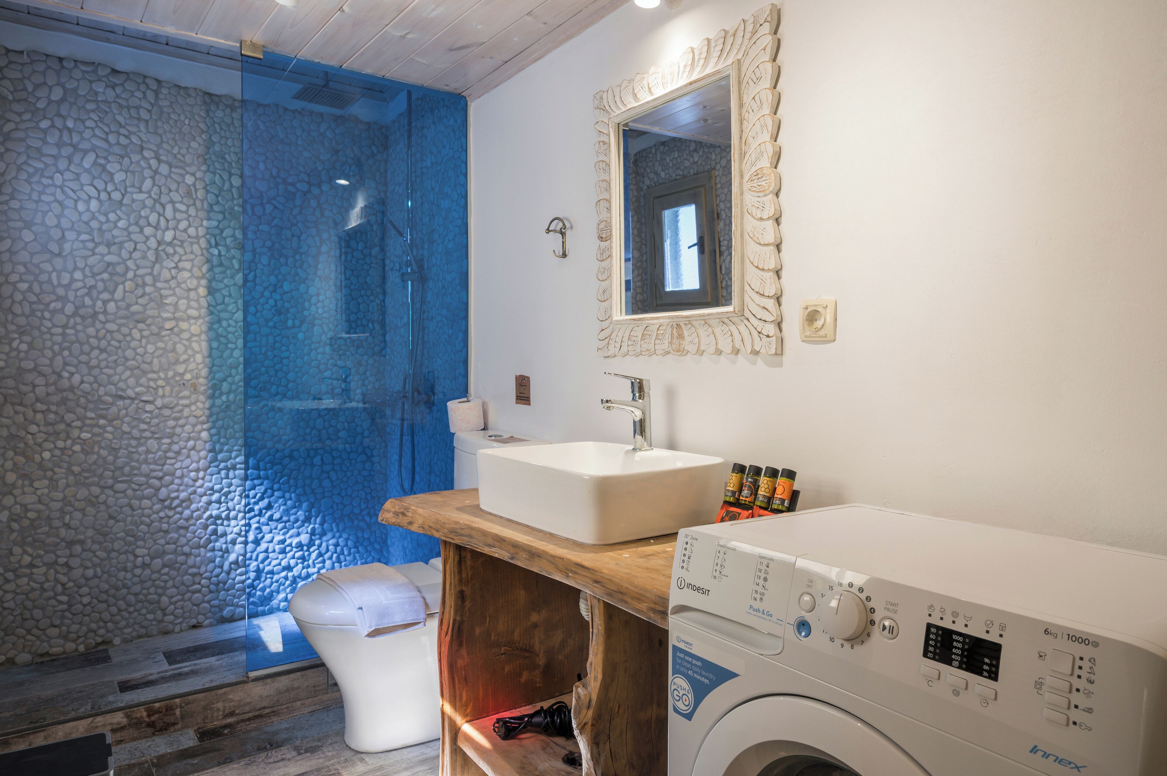A modern bathroom with a stone wall, a glass shower enclosure, a wooden vanity with a sink, and a front-loading washing machine.