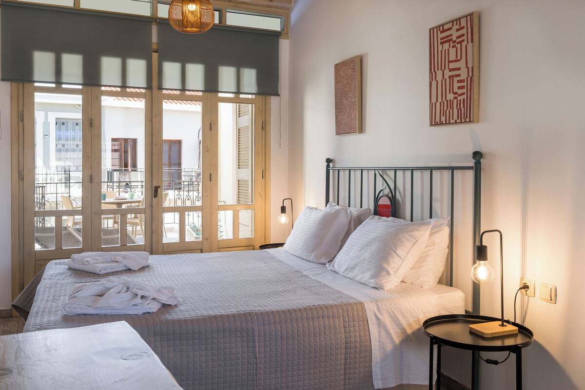 A bedroom with a bed, a bedside table with a lamp, and a view of a balcony.