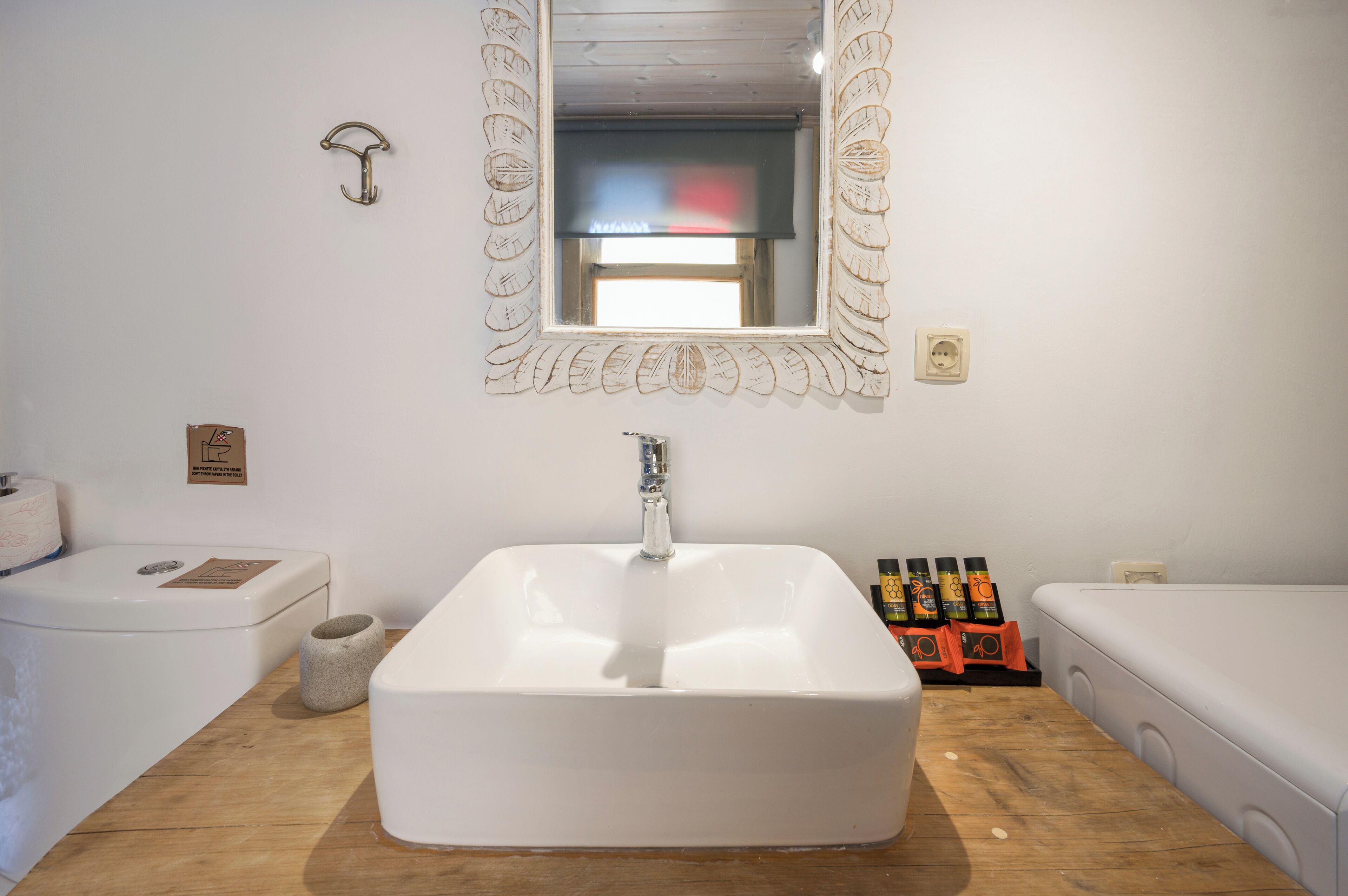 Une salle de bain avec un grand lavabo blanc, un miroir doté d’un cadre décoratif, un porte-serviettes et des toilettes.