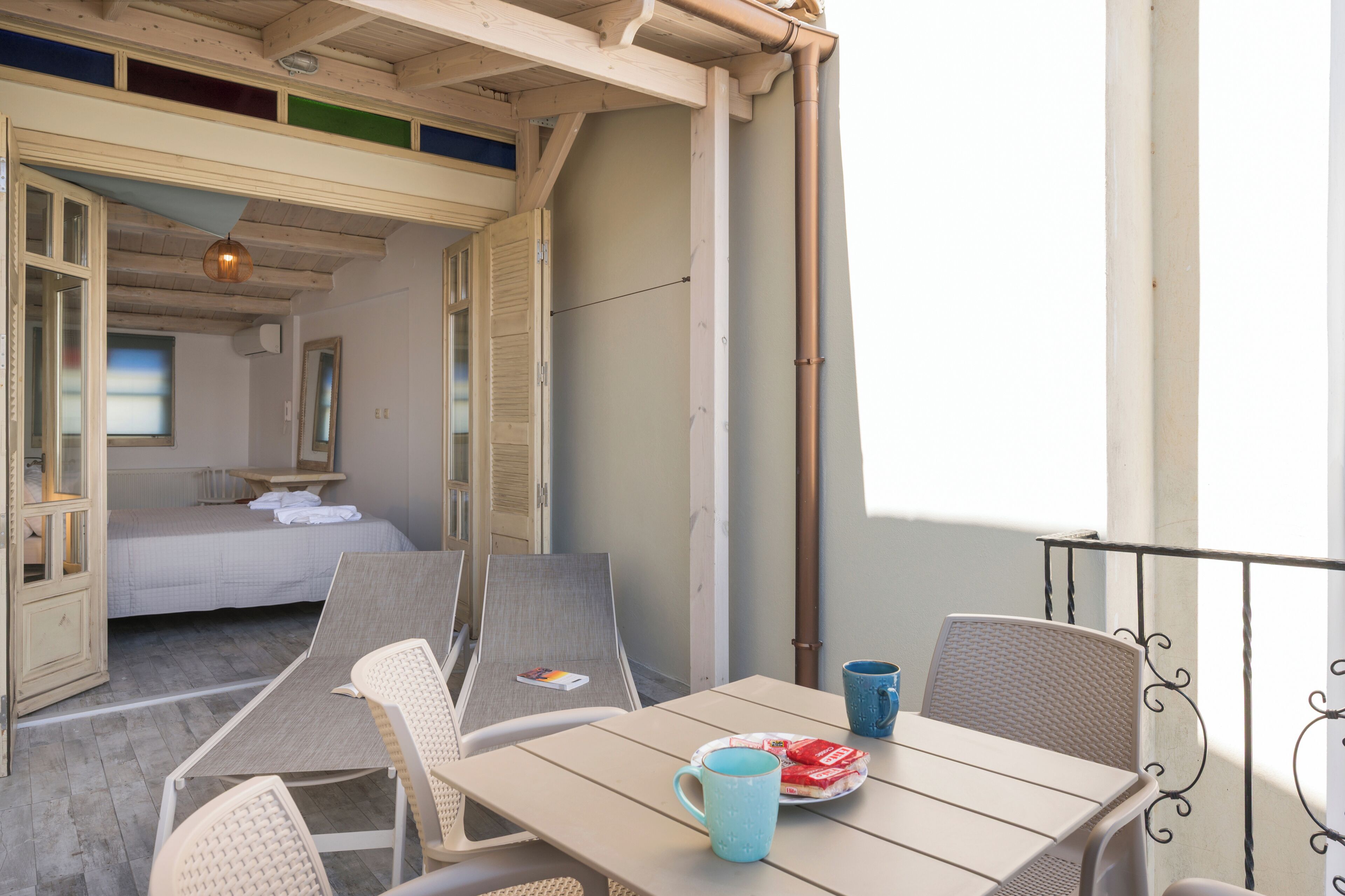 A room with a bed, a table with chairs, and a balcony with a railing.
