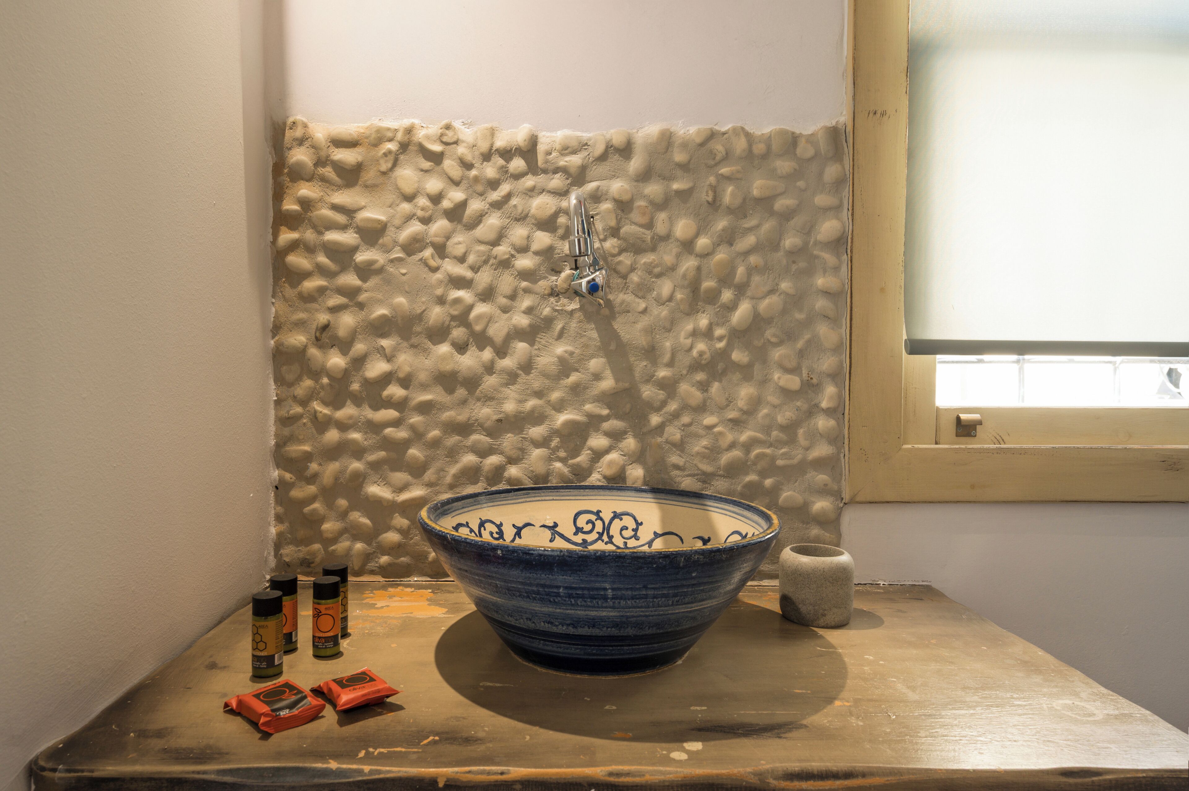 Casa de banho com lavatório cerâmico azul, parede com textura e janela.