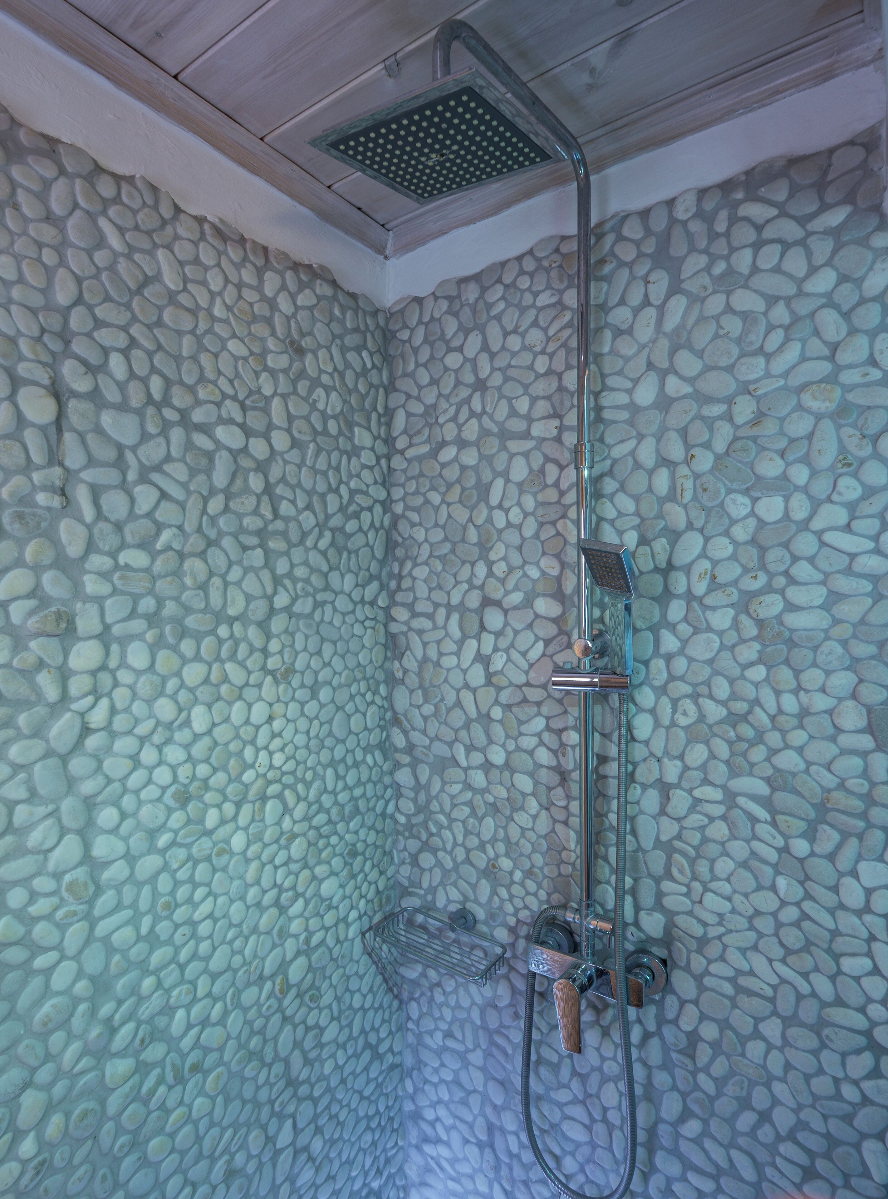 Ducha con pared de piedra, cabezal de ducha de mano y cabezal de ducha tipo lluvia.
