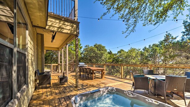 Une terrasse en bois avec un jacuzzi, du mobilier d’extérieur et une vue sur les arbres.