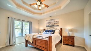Une chambre à coucher avec un lit en bois, une table de chevet, un ventilateur de plafond et une grande fenêtre avec des rideaux.