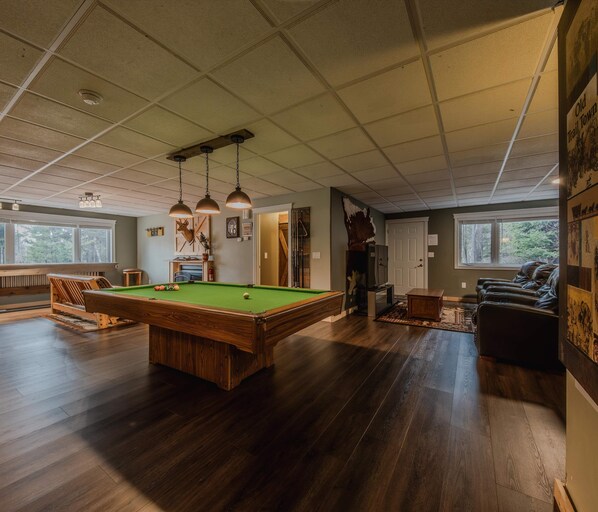 Amplia habitación con mesa de billar, piso de madera e iluminación colgante.