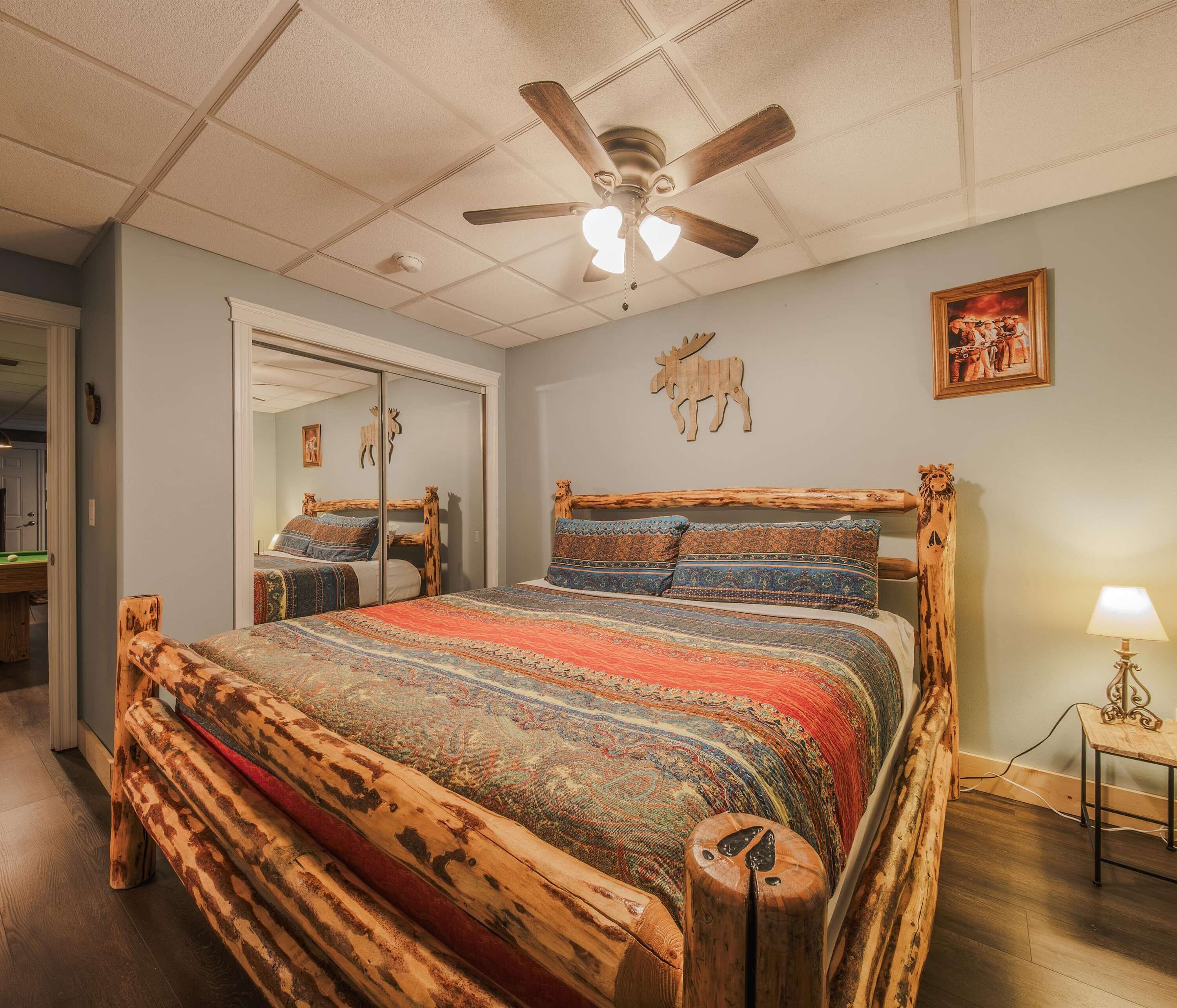 A bedroom with a wooden bed frame, a ceiling fan, a framed picture, and a lamp on a bedside table.