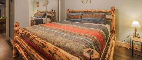 A bedroom with a wooden bed frame, a ceiling fan, a framed picture, and a lamp on a bedside table.