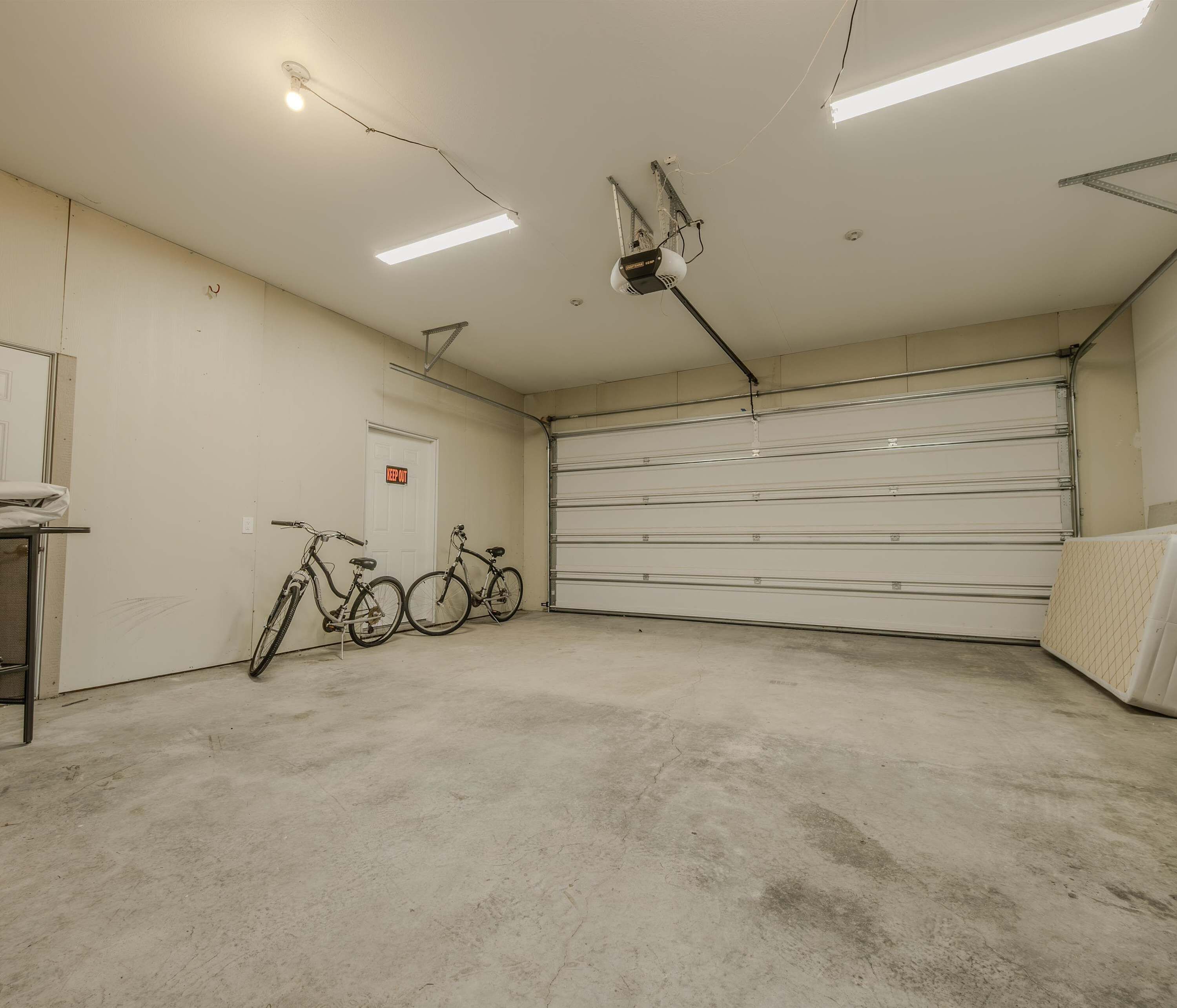 A garage with two bicycles, a closed garage door, and fluorescent lighting.
