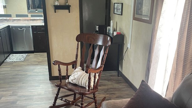 Un salon avec un fauteuil à bascule en bois, un canapé en cuir marron et une cuisine en arrière-plan.