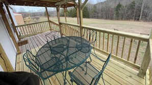 Une terrasse en bois avec une table et des chaises, donnant sur une pelouse et des arbres.