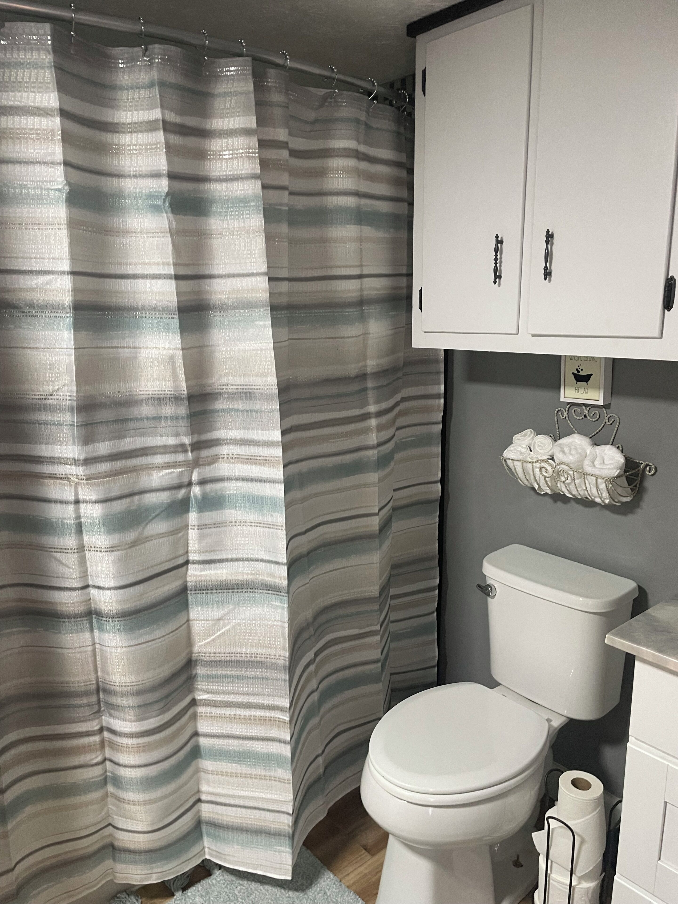 Une salle de bain avec un rideau de douche à rayures, des toilettes, un porte-serviettes avec des serviettes et un meuble sur lequel est apposée une étiquette.