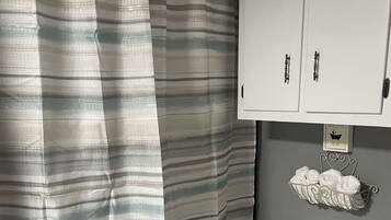 Une salle de bain avec un rideau de douche à rayures, des toilettes, un porte-serviettes avec des serviettes et un meuble sur lequel est apposée une étiquette.