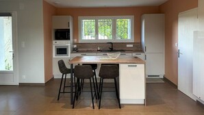 A modern kitchen with a central island, bar stools, and a window providing natural light. - L'ECRIN DE JOSELIA, 60m2 renovated family home in Périgord Vert (QUINSAC)