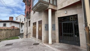 A building with a stone facade, a large metal gate, and a staircase leading to the entrance. - Apartment for 2 in the center of Nueva (Nueva de Llanes)