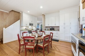 A modern kitchen with white cabinets, a wooden staircase, and a dining area with a round table and red chairs. - Another Glorious Day - Oceanfront w/Creek Dock (Pawleys Island)