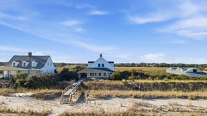 Une propriété située sur la côte, comprenant une maison principale et un bâtiment plus petit, reliés par une allée en bois.