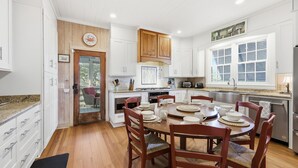Une cuisine moderne avec des meubles blancs, des éléments décoratifs en bois et un coin repas comprenant une table ronde et des chaises.