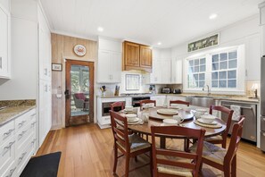 A modern kitchen with white cabinets, wooden accents, and a dining area with a round table and chairs. - Another Glorious Day - Oceanfront w/Creek Dock (Pawleys Island)