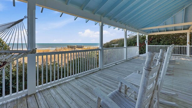 Une terrasse en bois avec des balustrades blanches, un hamac et une vue sur la plage et l’océan.