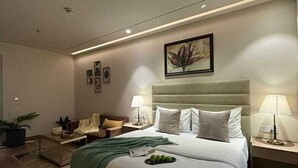 Un dormitorio moderno con una cama grande, dos mesitas de noche con lámparas, una manta verde y una obra de arte enmarcada en la pared.