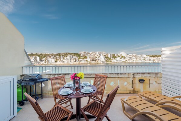 Une terrasse sur le toit avec une table dressée pour quatre personnes, un barbecue et des chaises longues.