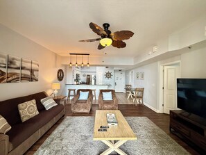 A living room with a brown sofa, a wooden coffee table, a ceiling fan, and a TV. - Beach Front Free round of Golf & Activities Daily! (Panama City Beach)