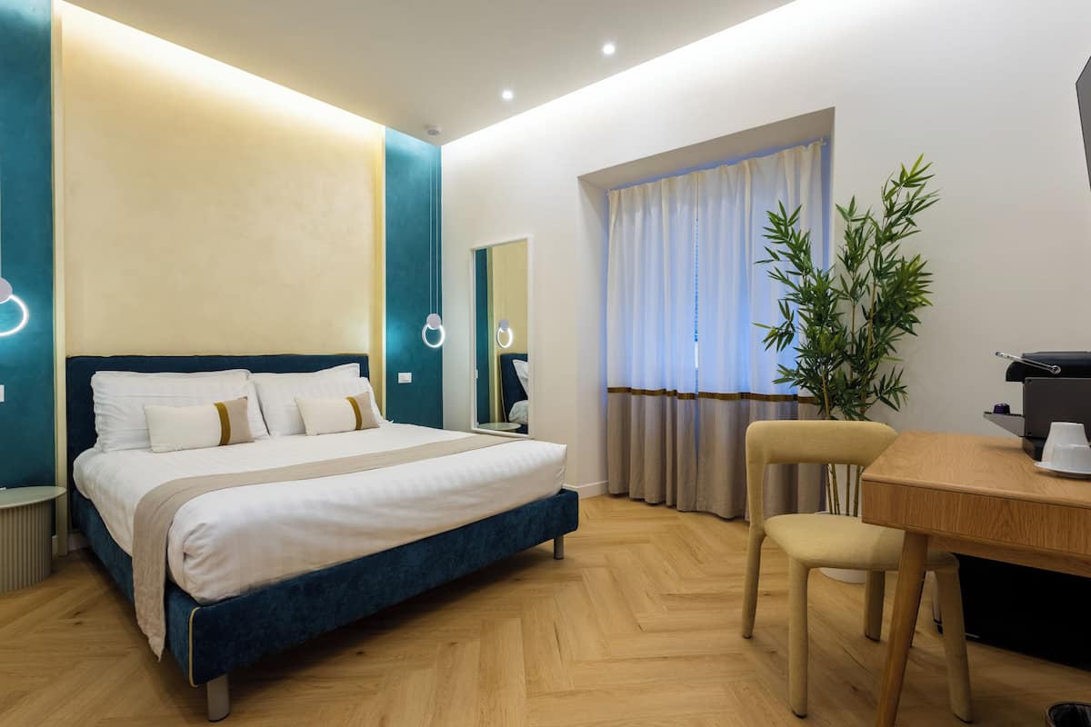 A modern hotel room with a large bed, a desk, and a potted plant.