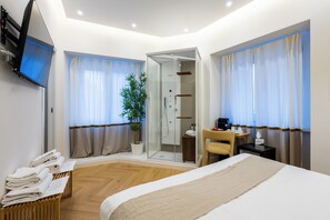 Ett hotellrum med en säng, ett skrivbord, en stol, en tv, en dusch och en krukväxt.