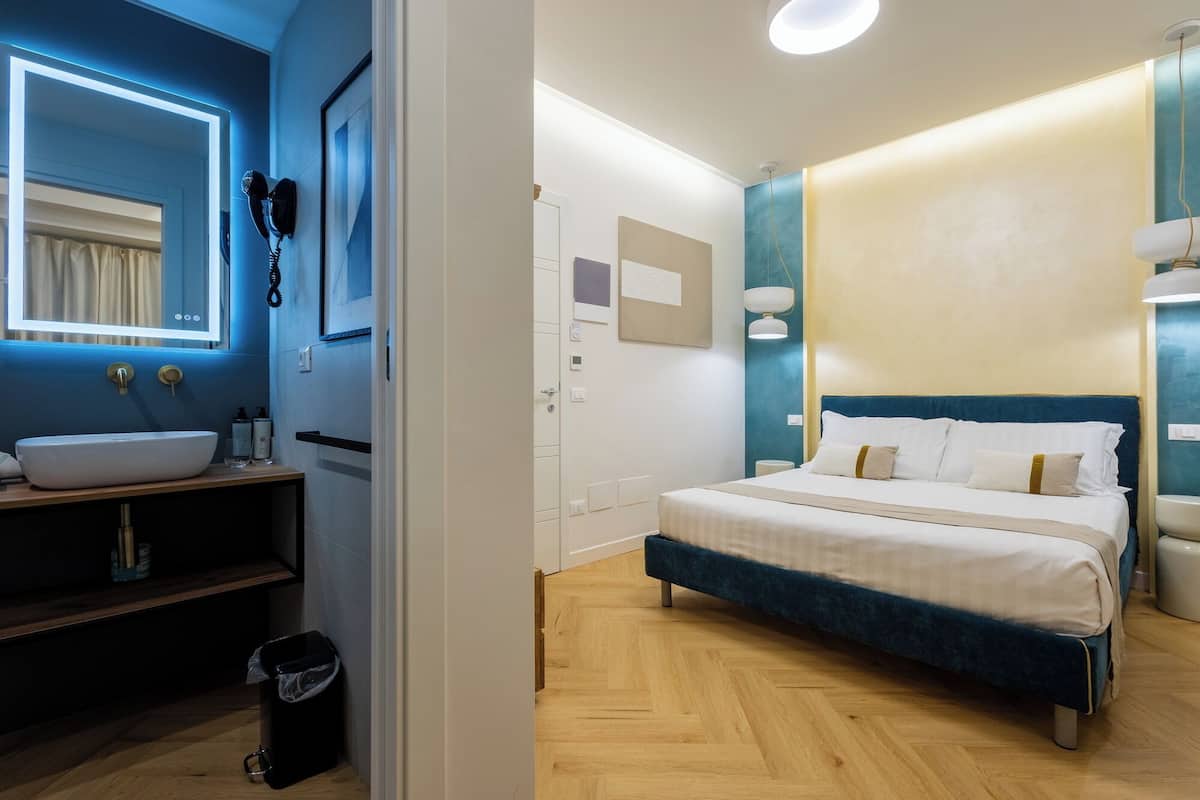 A modern bedroom with a large bed, a bedside table, a mirror, and a bathroom with a sink and toilet.