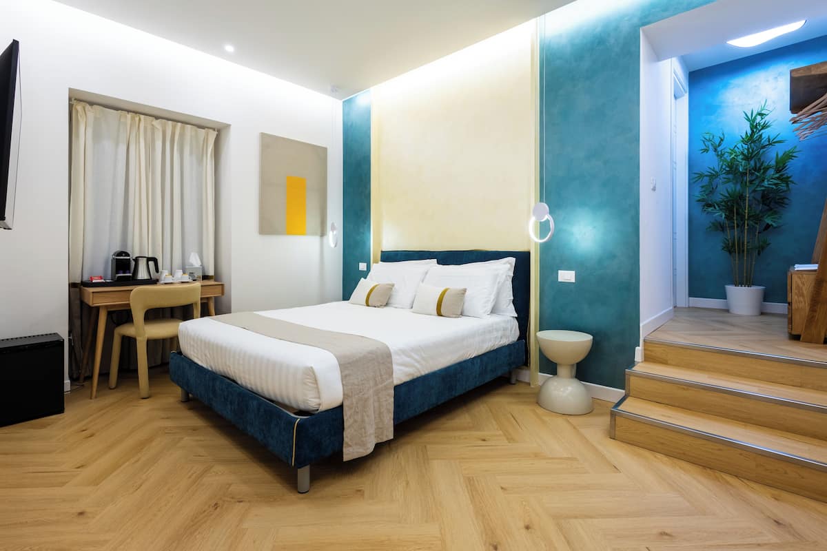 A modern hotel room with a bed, desk, chair, and a staircase leading to an upper floor.