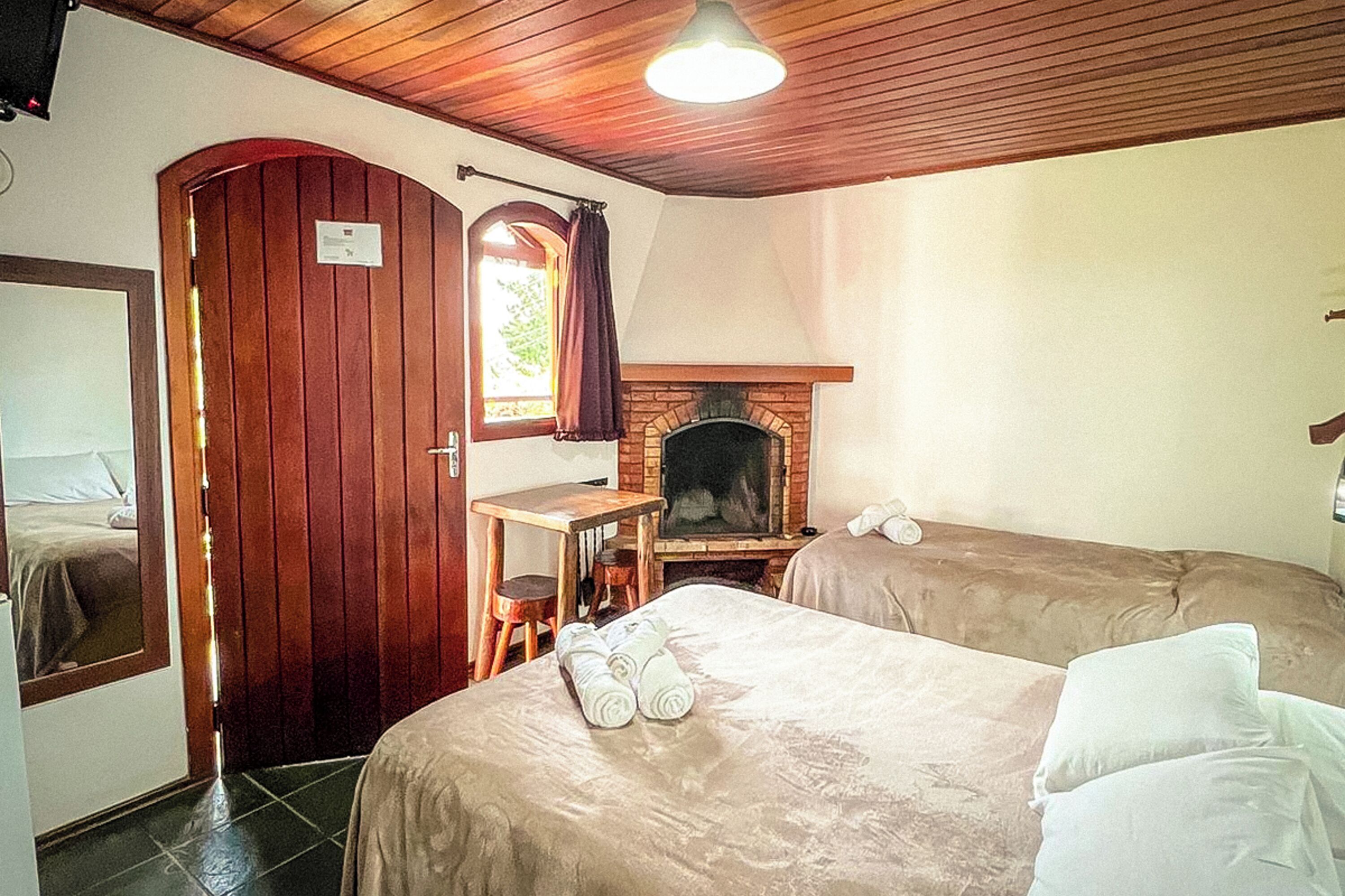 A room with two beds, a wooden door, a small table, a fireplace, and a mirror.