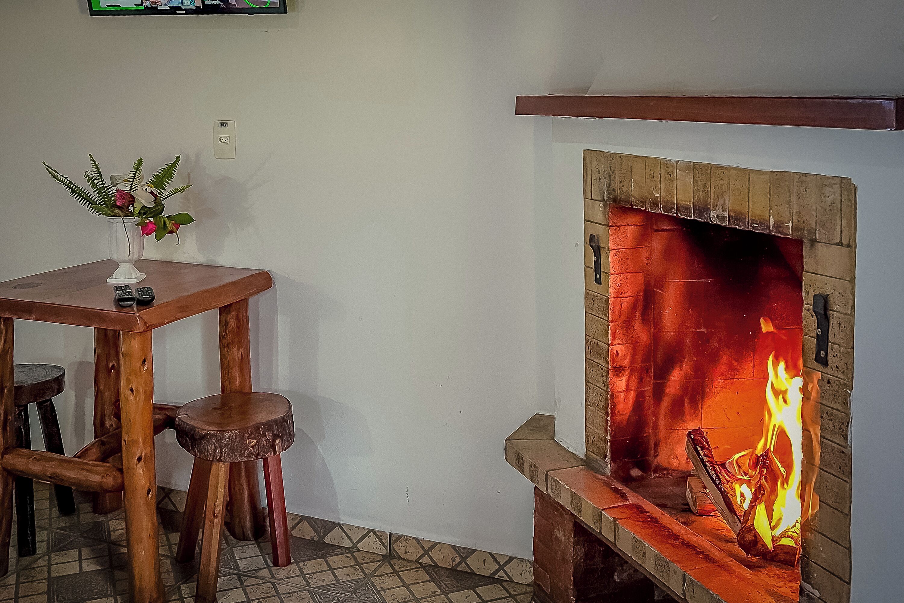 A fireplace with burning logs, a wooden table with a vase of flowers, and a tiled floor.