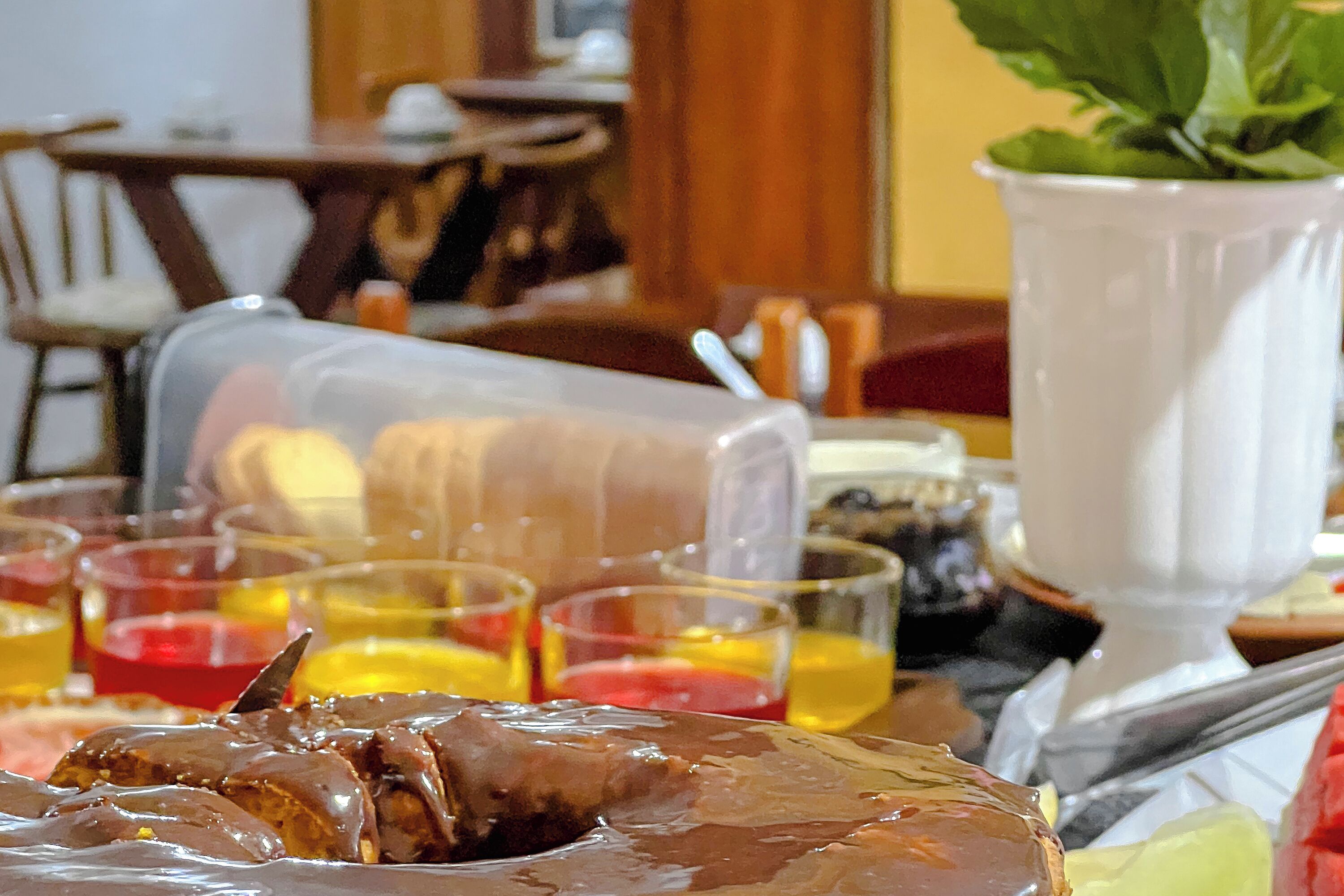 Uma mesa de jantar com um bolo coberto de chocolate, copos de bebidas e um jarro branco.