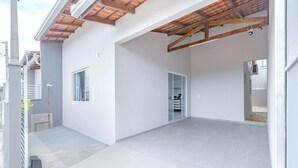 Un soggiorno open space con pavimento piastrellato, soffitto in legno e porta vetrata che conduce in un'altra stanza.