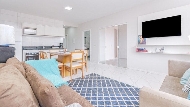 Un soggiorno moderno con un divano marrone, un tappeto azzurro decorato e una TV a parete.
