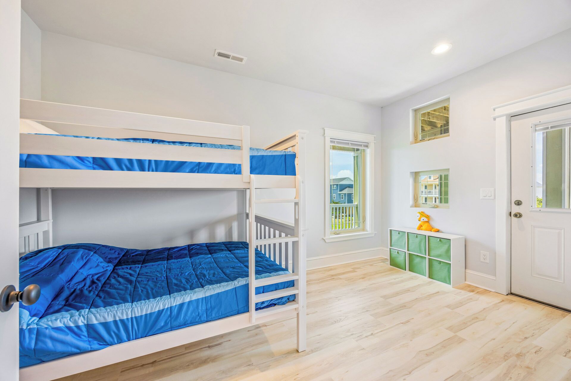 A room with bunk beds, a small window, a door, and a green storage unit.